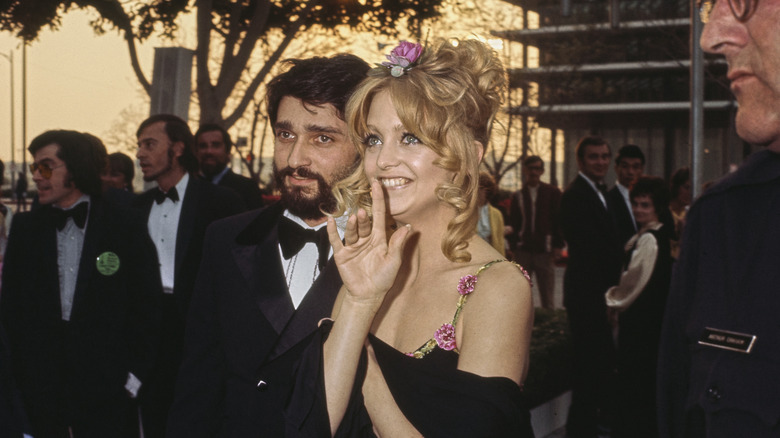Goldie Hawn lleva una flor en el pelo y un vestido negro con tirantes florales en 1973