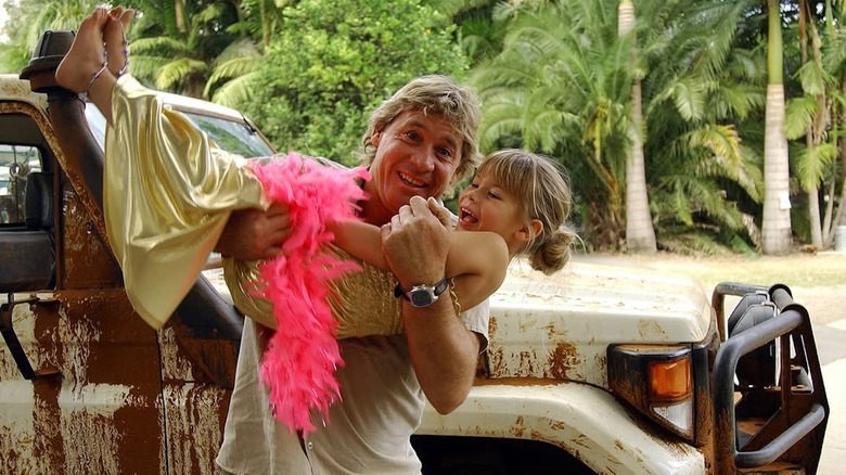 Steve Irwin sostiene a Bindi Irwin, que está vestida con una boa de plumas rosa.