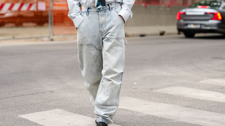 Primer plano de las piernas de alguien mientras camina con jeans lavados con ácido y una camisa blanca.