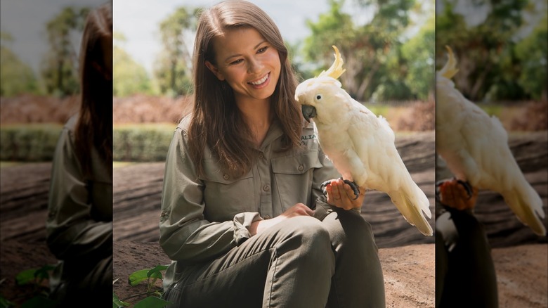Bindi Irwin vestida completamente de color caqui, sosteniendo un pájaro en el zoológico de Australia.