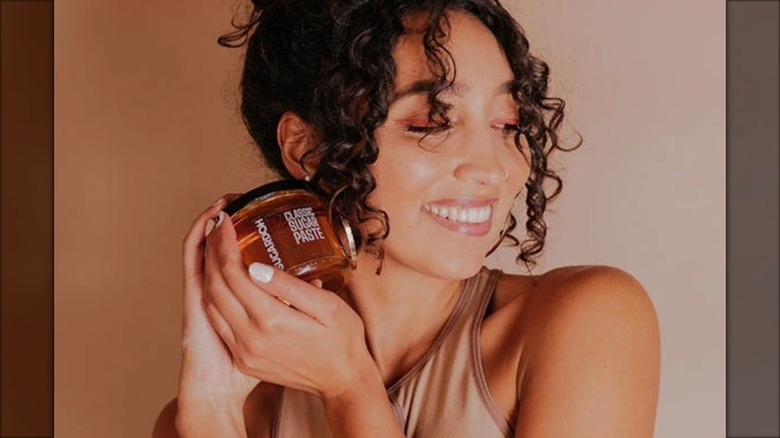 La fundadora de Sugardoh, Aliyah Marandiz, posa con un frasco de pasta depilatoria junto a la cara.