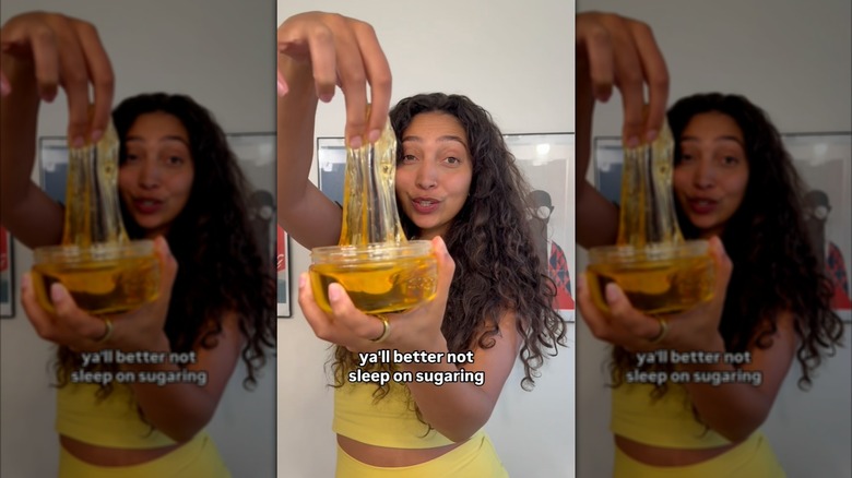 Imagen fija de un video de Instagram de Aliyah Marandiz vistiendo un traje amarillo y sosteniendo un frasco de producto depilatorio Sugardoh.