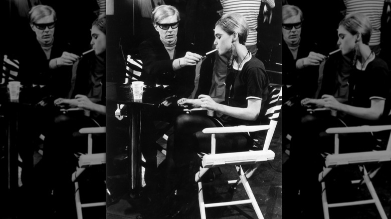 El artista pop estadounidense Andy Warhol sentado junto a la actriz Edie Sedgwick y encendiendo su cigarrillo en el set de una de sus películas en 1965.