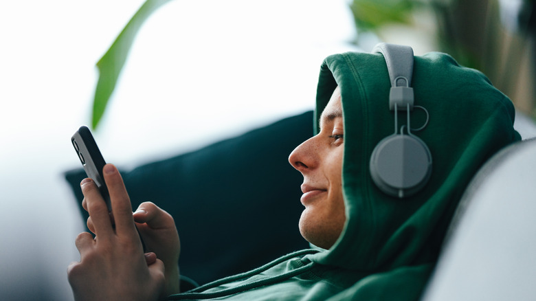 Un joven con auriculares y escribiendo en su teléfono inteligente
