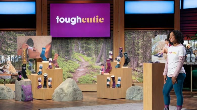 La fundadora de ToughCutie, Brittany Coleman, viste una camiseta blanca con el logotipo de su empresa sobre una camisa rosa con capucha de manga larga, jeans y sus calcetines ToughCutie mientras presenta su negocio en Shark Tank, que se transmitirá en enero de 2025.