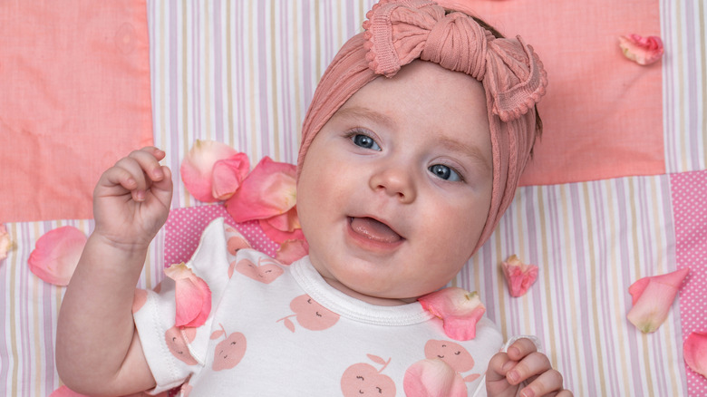 Un bebé con un lazo rosa en la cabeza con pétalos esparcidos