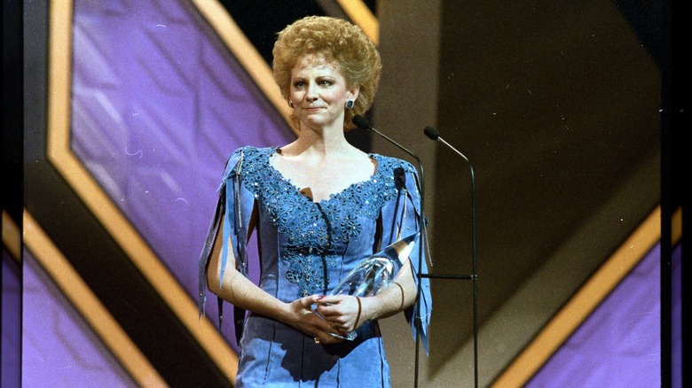 Reba McEntire con un peinado corto y voluminoso luciendo un vestido azul en el escenario de los Premios de la Asociación de Música Country en 1986.
