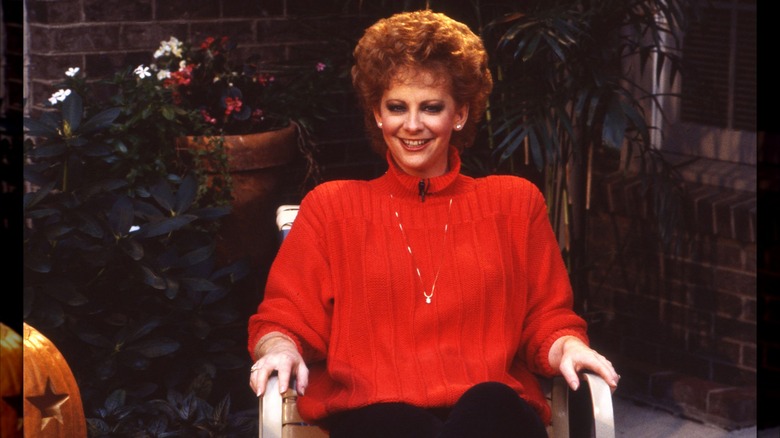 Reba McEntire con un suéter rojo voluminoso y un peinado corto y voluminoso en 1987.