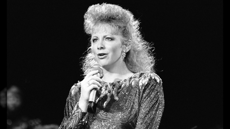 Reba McEntire con un top brillante y el cabello recogido actuando en 1988.