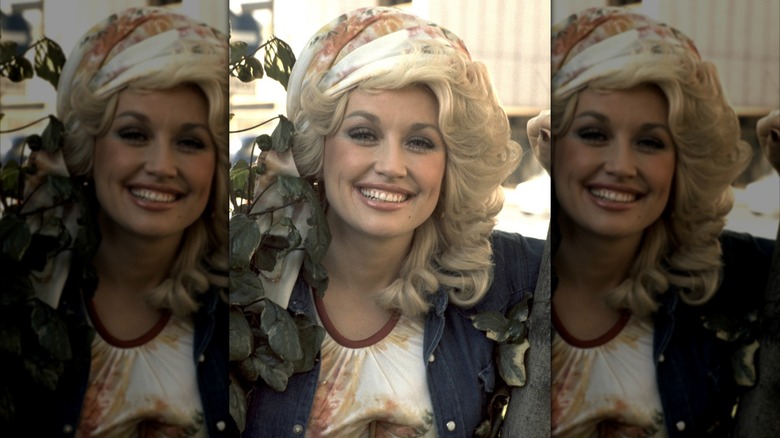 Dolly Parton sonriendo con un pañuelo en la cabeza y una chaqueta vaquera.