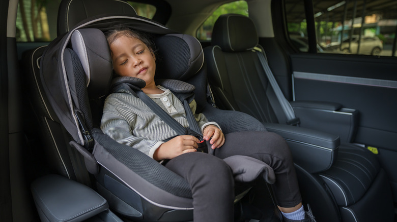 Niña preescolar sentada y durmiendo en el asiento del auto, silla de seguridad para bebé viajando