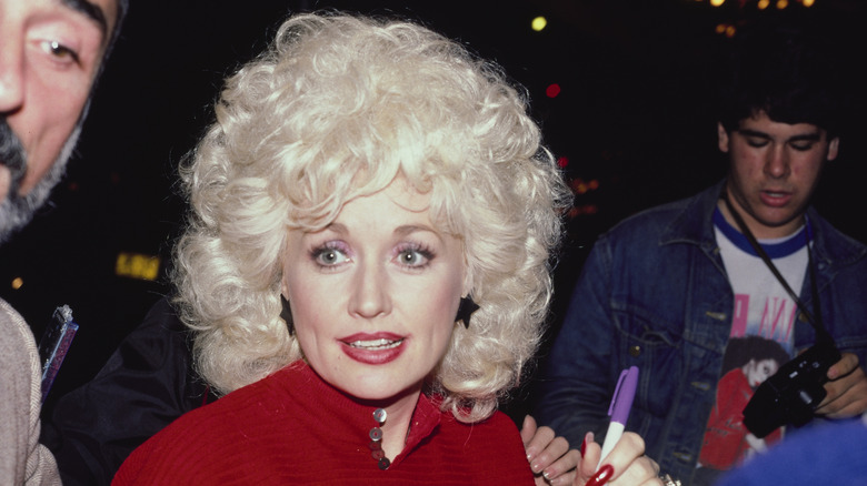 Dolly Parton firmando autógrafos en 1984 luciendo un top rojo con aretes en forma de estrella.