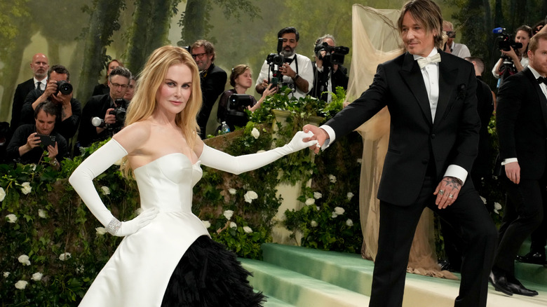 Nicole Kidman posando con un vestido blanco sin tirantes y guantes de ópera blancos tomando la mano de Keith Urban en un evento en 2024.