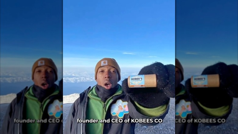 Kobe Harris en las montañas nevadas sosteniendo un bálsamo labial Kobee