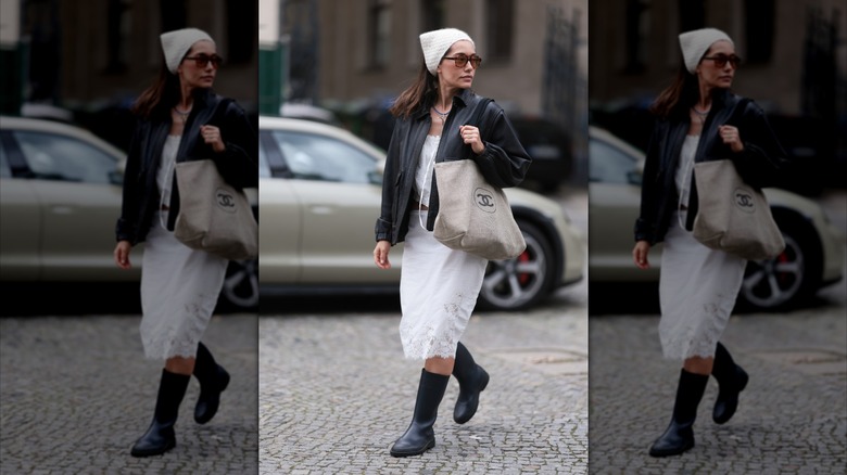Una mujer con botas de lluvia negras y una falda midi blanca.