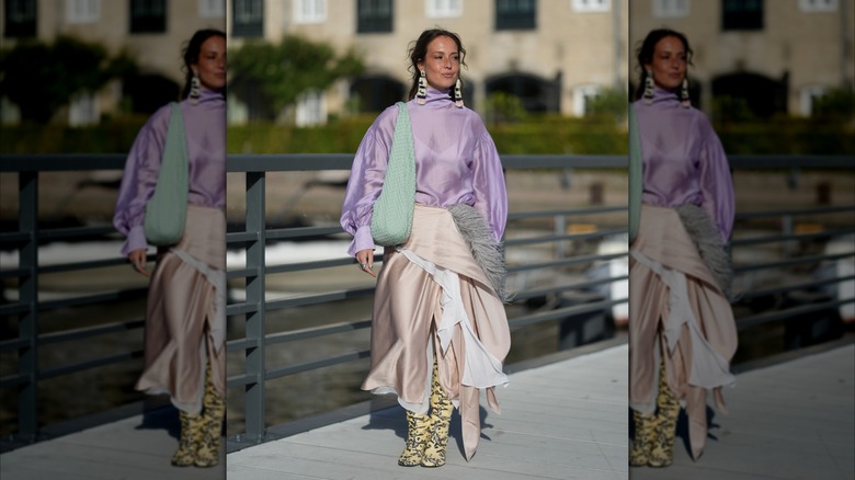 Una mujer que llevaba botas de piel de serpiente de color amarillo neón y una falda cruzada de color rosa pálido.