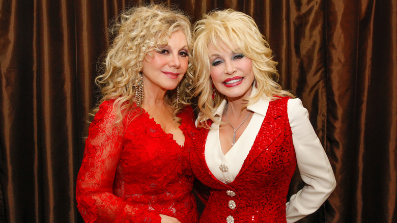 Stella Parton y Dolly Parton posan juntas con trajes rojos brillantes a juego.