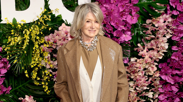 Martha Stewart posando en un evento en 2026 vistiendo un conjunto beige y blanco con un collar llamativo.