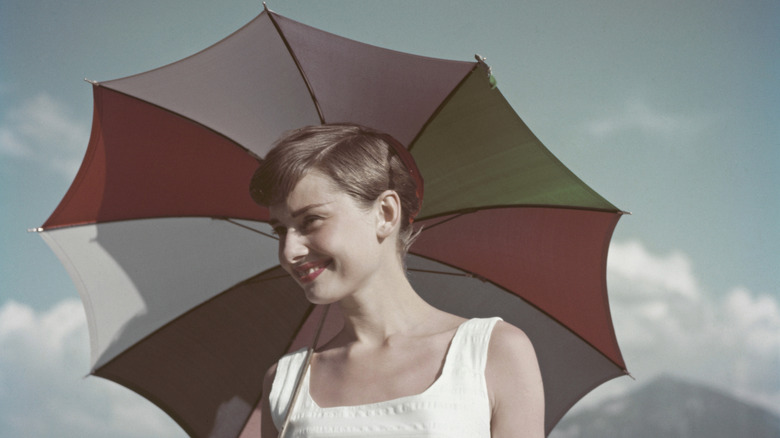 Audrey Hepburn sonriendo bajo un paraguas de colores