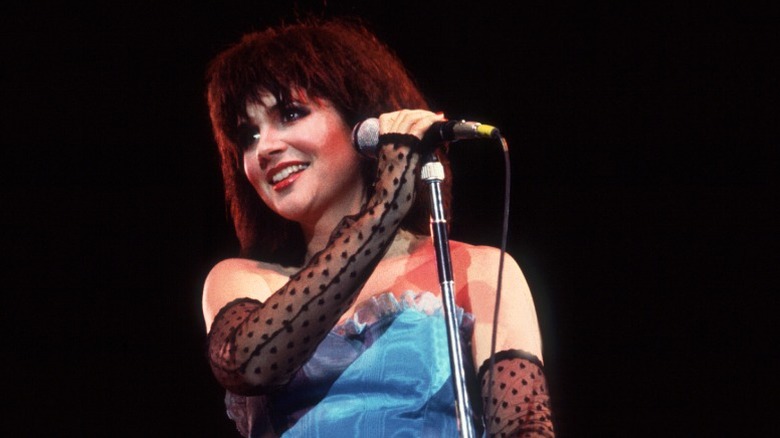 Linda Ronstadt con un top azul sin tirantes y guantes transparentes sin dedos mientras actuaba en los años 80