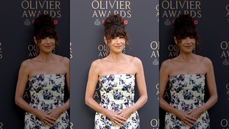 Minnie Driver posando en un evento luce un vestido palabra de honor con estampado de flores y el pelo recogido.