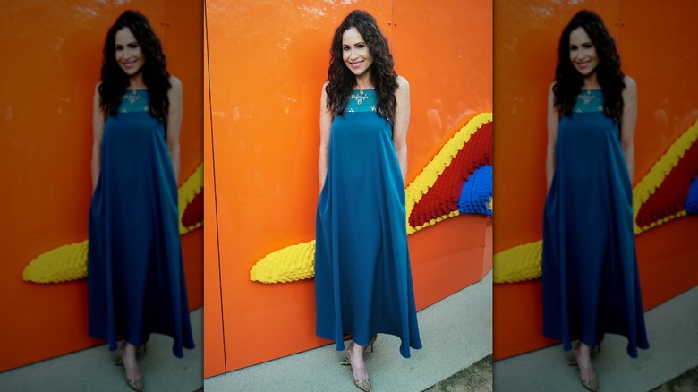 Minnie Driver en un evento con un vestido azul holgado y el pelo medio recogido y medio suelto.