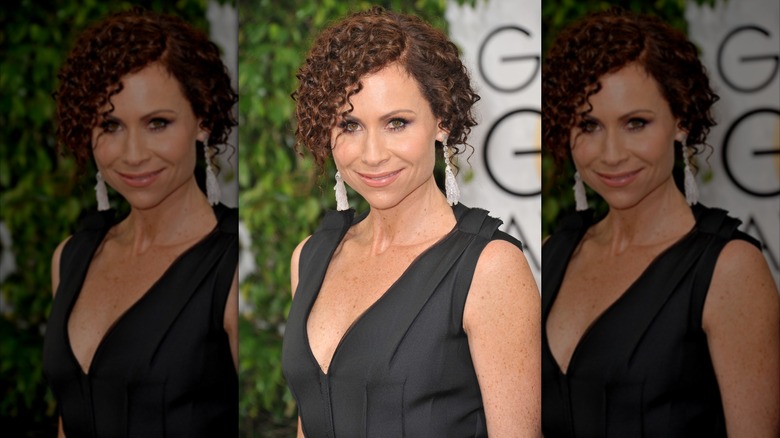 Minnie Driver posando en los Globos de Oro con un vestido negro y el pelo muy rizado y recogido.