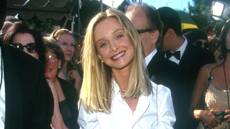 Calista Flockhart sonriendo en un evento de alfombra roja con el pelo hasta la mitad y vistiendo una camisa blanca.