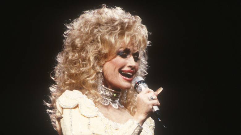 Dolly Parton canta frente a un micrófono con el pelo rubio y rizado