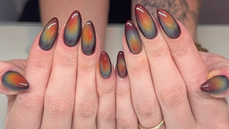 Manos con uñas de aura en tonos tierra.