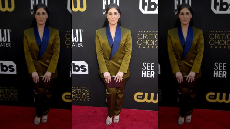 Mayim Bialik sonríe con un traje dorado y azul en la alfombra roja.