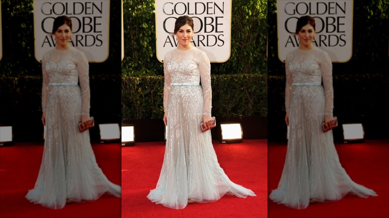 Mayim Bialik sonríe con un vestido plateado transparente adornado en la alfombra roja.