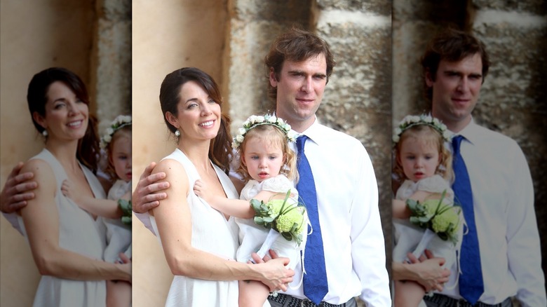Michelle Morgan sostiene a su hija Mara con su esposo Derek de pie con el brazo alrededor de la parte superior de su espalda.