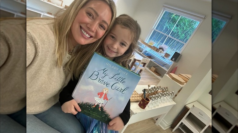 Hilary Duff lleva su cabello rubio liso hacia abajo con un suéter beige y jeans mientras posa con su hija Banks y su nuevo libro.