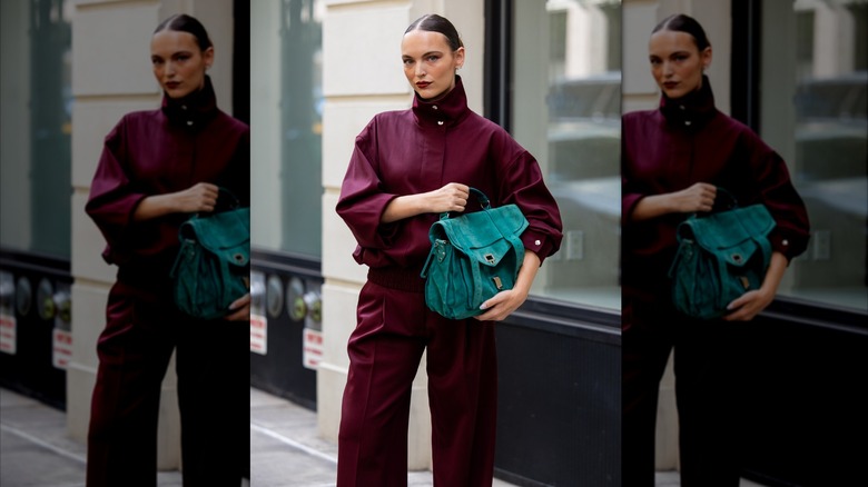 Mujer vestida con un traje burdeos sosteniendo una bolsa verde