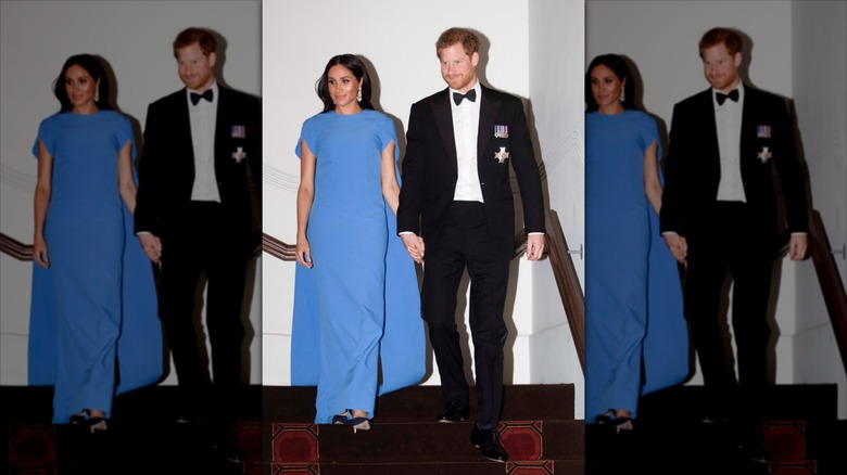 Meghan Markle con un vestido de capa azul junto al príncipe Harry con esmoquin