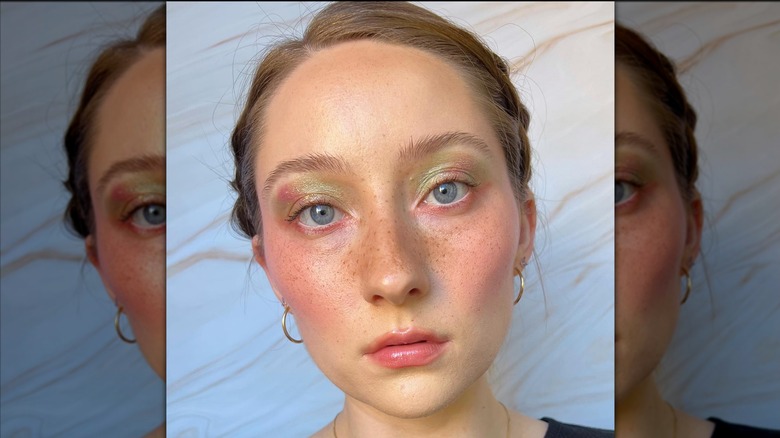 Una persona con pecas y maquillaje de ojos radiante posando para una foto.