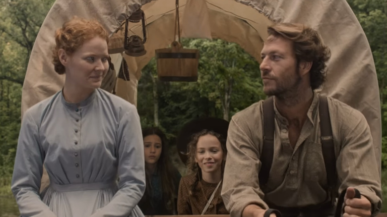 Luke Bracey y Crosby Fitzgerald se miran en la parte delantera de una carreta con los personajes Laura y Mary detrás de ellos en 'La casa de la pradera' de Netflix.