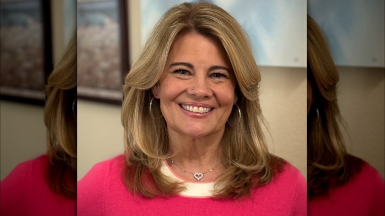 Lisa Whelchel sonríe para una foto con un suéter rosa y joyas plateadas