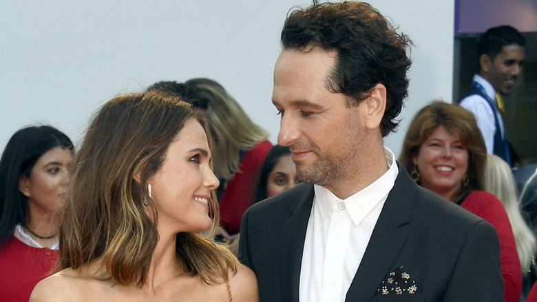 Keri Russell y Matthew Rhys sonríen mientras se miran afectuosamente en un evento de alfombra roja al aire libre.