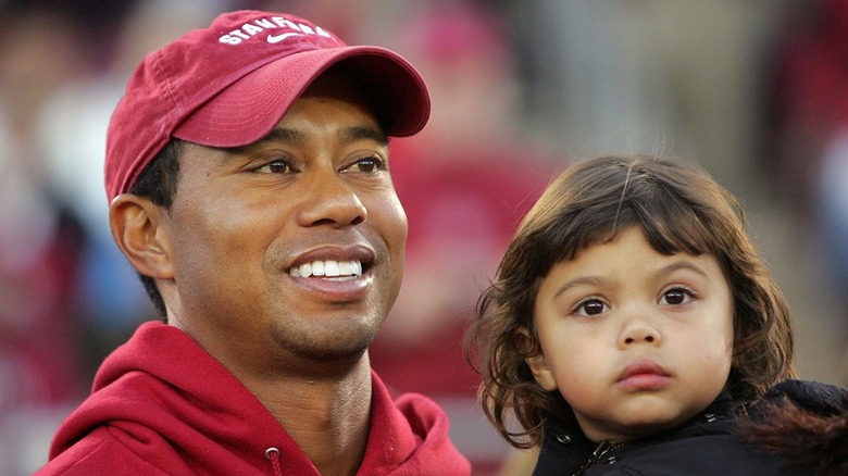 Tiger Woods sostiene a su hija pequeña Sam Woods con una chaqueta negra y el cabello castaño suelto mientras asiste a un partido de fútbol de Stanford en 2009.