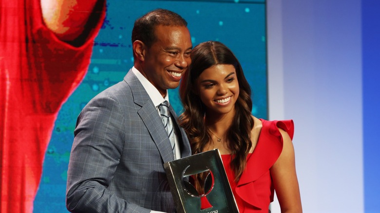 Sam Woods posa con su padre con el cabello suelto en ondas sueltas con raya en medio y un vestido rojo brillante sin mangas mientras asiste a la ceremonia de incorporación al Salón de la Fama del Golf Mundial en Florida en 2022.