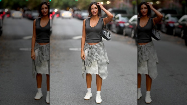 Una mujer vestida con falda y camiseta sin mangas con zapatillas y calcetines blancos.