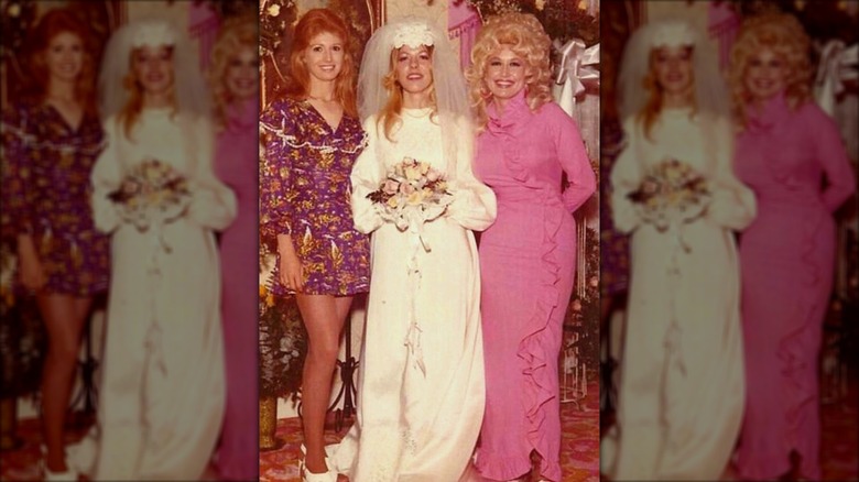 Judy Ogle (izquierda) con un vestido morado con cabello largo pelirrojo junto a Freida Parton (centro) y Dolly Parton (derecha)