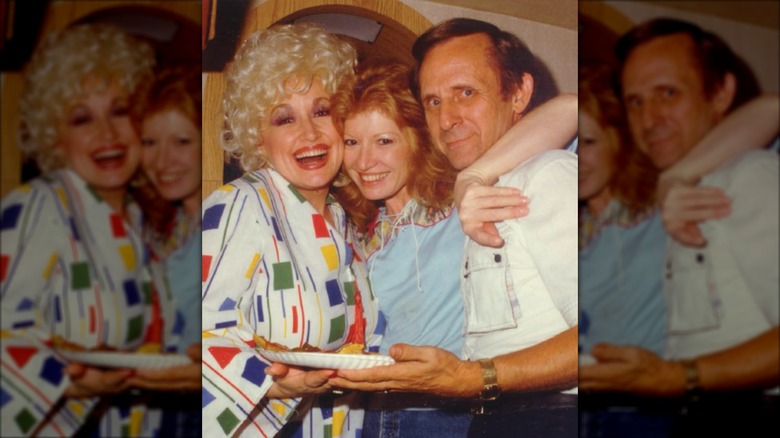 Dolly Parton (izquierda) abraza a Judy Ogle (centro), que viste un top azul claro y un bob pelirrojo.