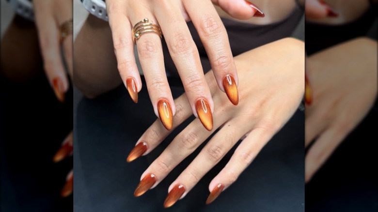Manicura ojo de gato con diseños en naranja y ámbar.