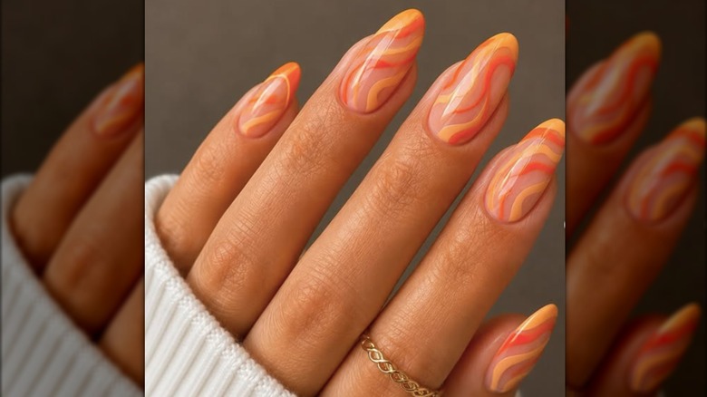 Manicura en forma de almendra pintada con remolinos de esmalte naranja claro y oscuro.