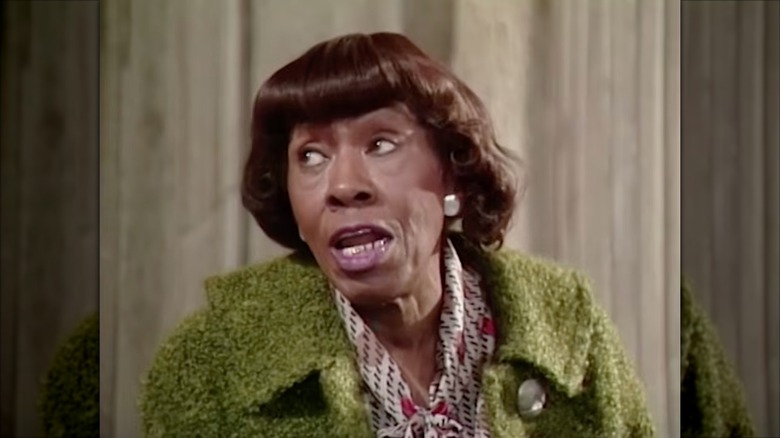 Helen Martin con un abrigo verde y una blusa color crema estampada.