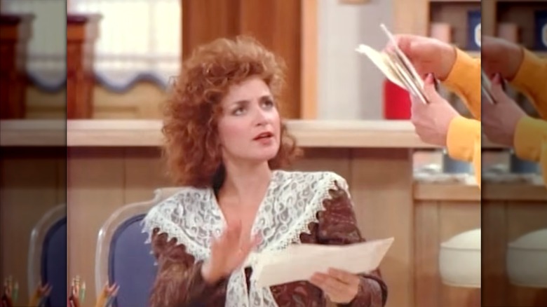Annie Potts con una blusa marrón con adornos de encaje y cabello rojo rizado