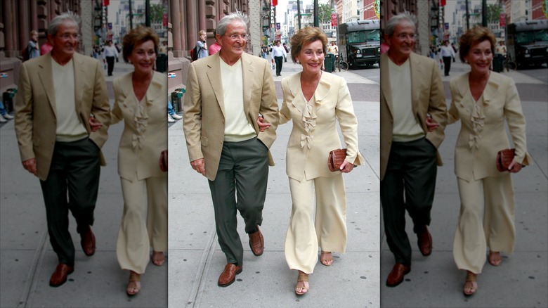 Judy Sheindlin camina con su marido (izq.) vistiendo pantalones anchos y una blusa con volantes.